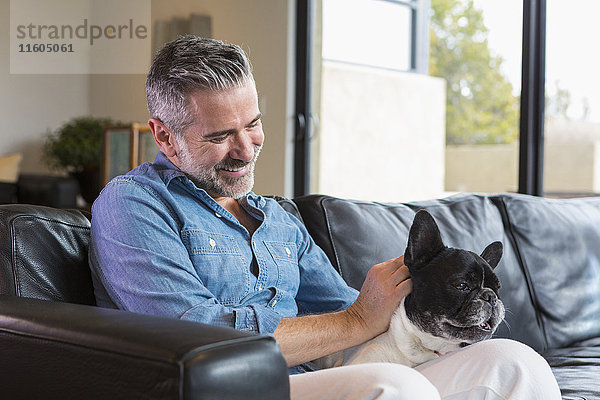 Kaukasischer Mann sitzt auf Sofa und streichelt Hund