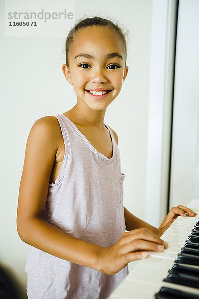 Lächelndes Mixed-Race-Mädchen spielt Musik auf einem Keyboard