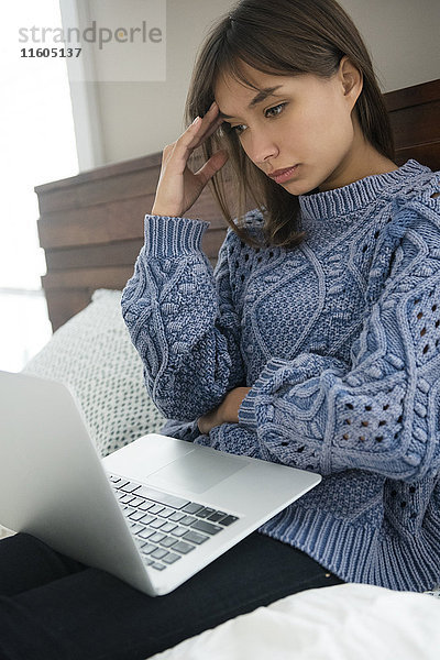 Frustrierte gemischtrassige Frau benutzt Laptop im Bett