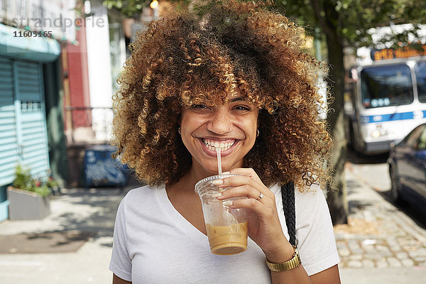 Schwarze Frau trinkt mit Strohhalm auf dem Bürgersteig der Stadt