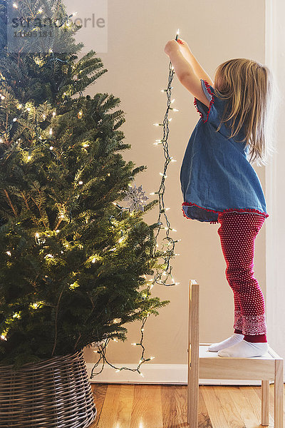 Kaukasisches Mädchen hängt Lichter am Weihnachtsbaum auf