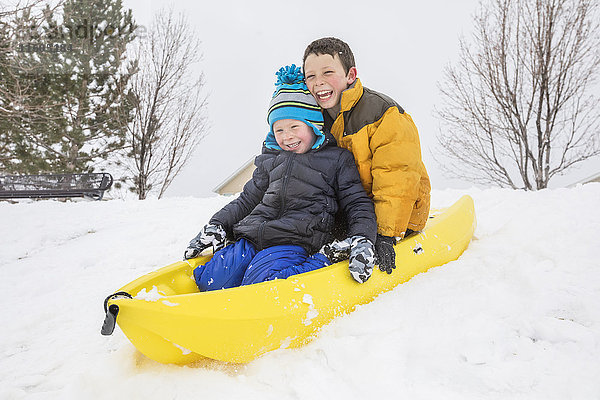 Lächelnde Jungen rutschen auf Schlitten auf einem Hügel im Winter