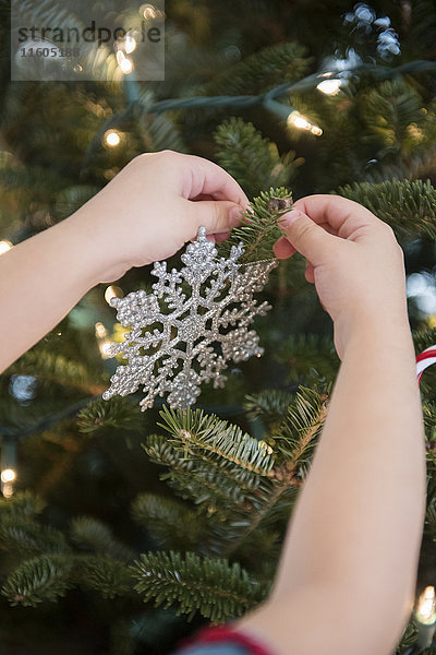 Kaukasisches Mädchen hängt Schneeflocke Ornament auf Weihnachtsbaum