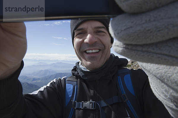 Hispanischer Mann posiert für Handy-Selfie auf einem Berg