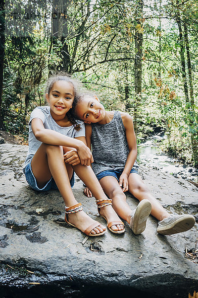 Porträt von lächelnden Mixed-Race-Mädchen  die auf einem Felsen sitzen