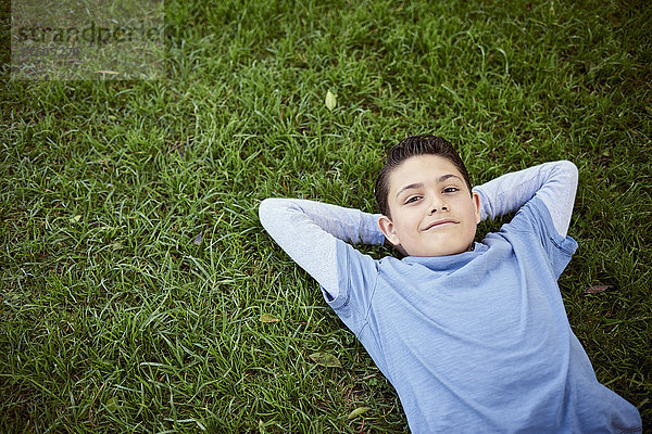 Lächelnder hispanischer Junge  der im Gras liegt