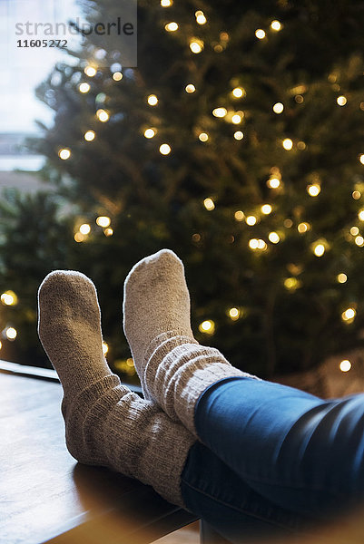 Socken einer kaukasischen Frau mit Füßen auf dem Tisch neben dem Weihnachtsbaum