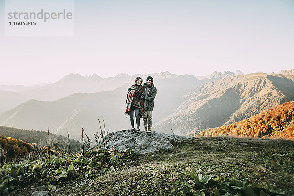 Kaukasisches Paar steht auf einem Bergfelsen mit Blick auf ein Tal