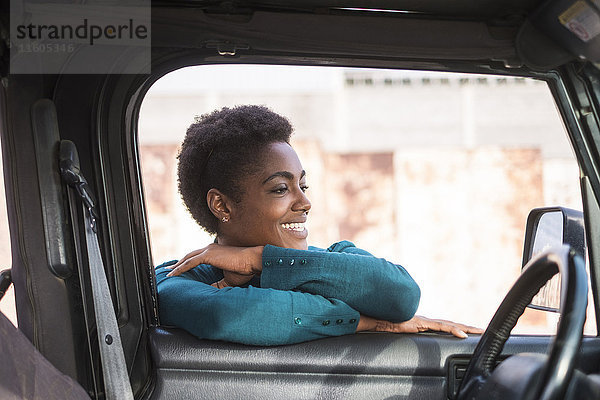 Lächelnde afroamerikanische Frau  die sich an ein Autofenster lehnt