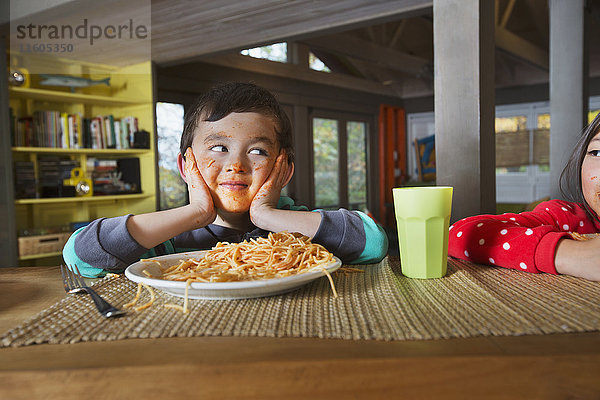 Schwester beobachtet Mixed Race Bruder mit unordentlichem Gesicht essen Spaghetti