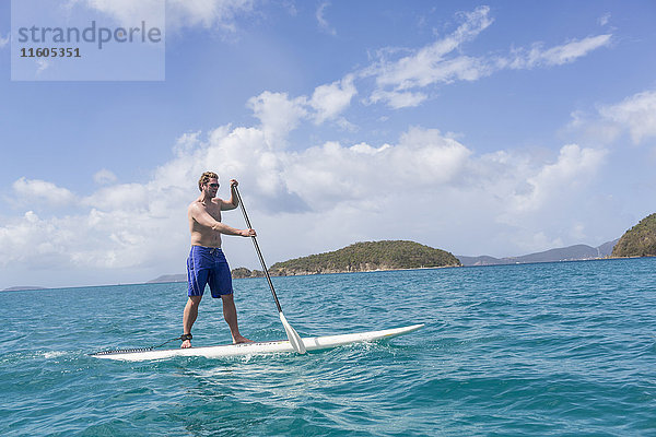 Kaukasischer Mann steht auf einem Paddelbrett auf dem Meer
