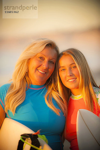 Porträt einer lächelnden kaukasischen Mutter und ihrer Tochter  die ein Surfbrett halten