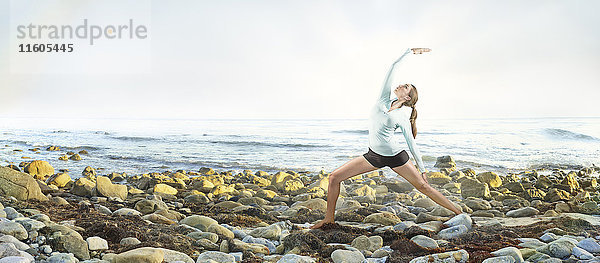 Gemischtrassige Frau übt Yoga am felsigen Strand