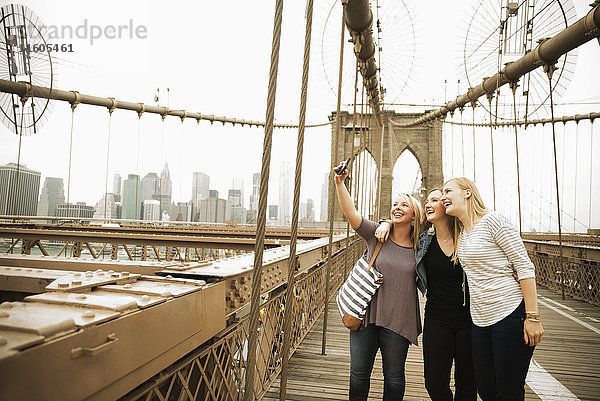 Lächelnde kaukasische Frauen posieren für ein Handy-Selfie auf einer Brücke