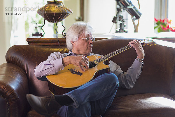 Kaukasischer Mann spielt Gitarre auf Sofa