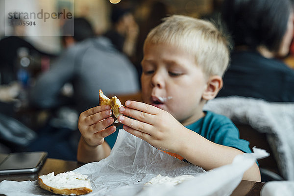 Gemischtrassiger Junge isst unordentlichen Bagel im Restaurant