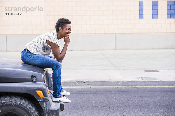 Lächelnde afroamerikanische Frau auf der Motorhaube eines Autos sitzend