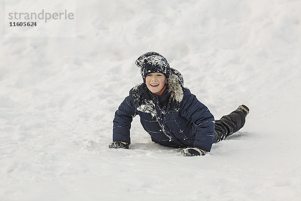 Fröhlicher Junge schaut weg  während er im Schnee liegt.