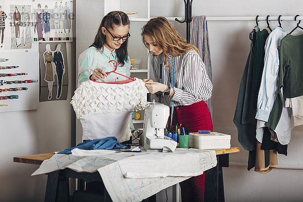 Praktikantin untersucht Kleiderstoff von Designerin mit Kleiderbügel im Modestudio