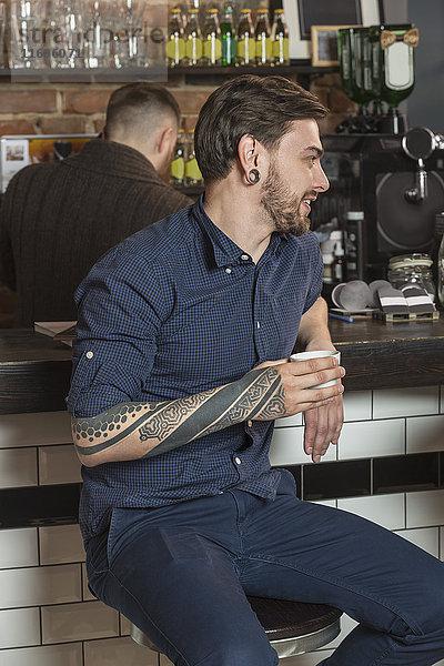 Fröhlicher Friseur sitzend mit Kaffee an der Bar im Friseursalon