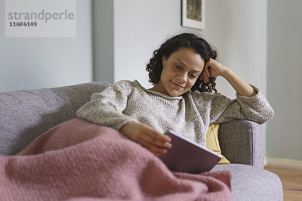 Lächelnde Frau mit digitalem Tablett beim Entspannen auf dem Sofa zu Hause