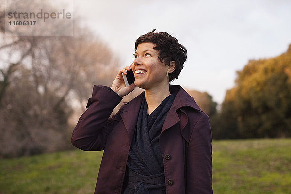Fröhliche erwachsene Frau mit Smartphone auf dem Feld