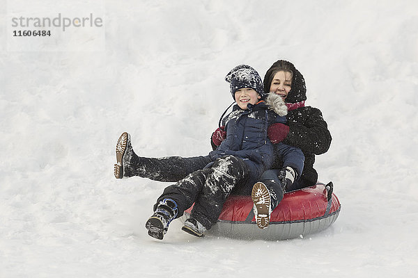 Porträt einer glücklichen Großmutter und eines Enkels auf einem aufblasbaren Ring im Schnee.