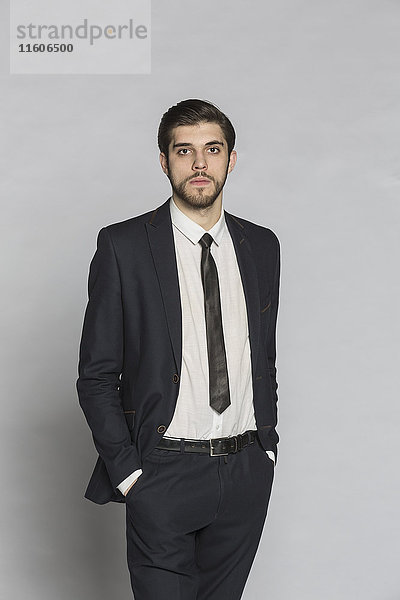 Porträt eines selbstbewussten Geschäftsmannes mit Händen in den Taschen vor grauem Hintergrund