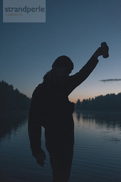 Silhouette der Frau mit Getränkedose am See bei Sonnenuntergang