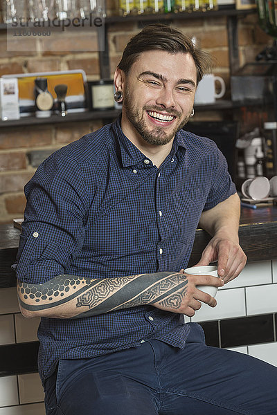 Porträt eines fröhlichen Friseurs mit Kaffee an der Bar im Friseursalon