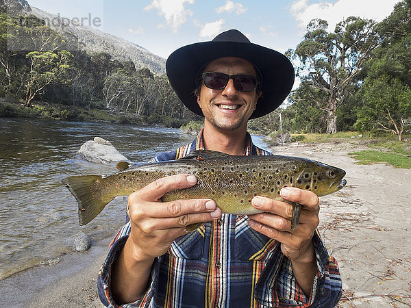 Porträt eines glücklichen reifen Mannes mit Fisch am Fluss  Jindabyne  New South Wales  Australien