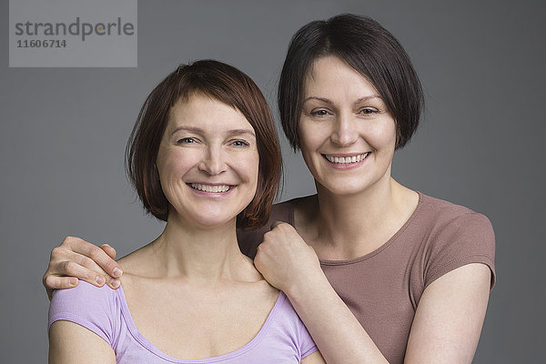 Portrait von glücklichen reifen Freundinnen vor grauem Hintergrund