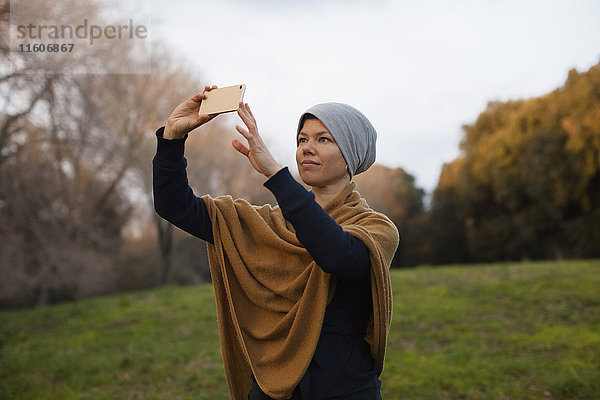 Mittlere erwachsene Frau beim Fotografieren durch Smartphone auf dem Feld gegen den Himmel