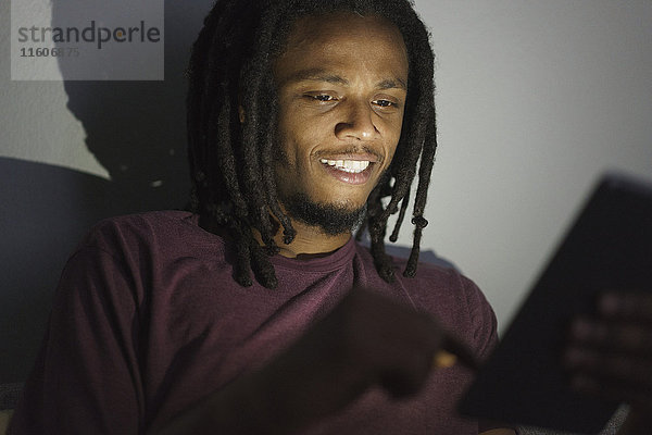 Junger Mann mit digitalem Tablett in der Dunkelkammer zu Hause
