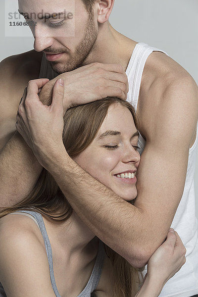 Mann umarmt lächelnde Freundin vor grauem Hintergrund