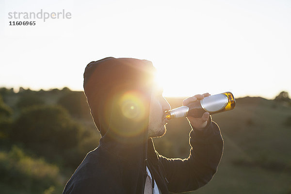 Seitenansicht des Mannes mit Biertrinken auf dem Feld bei Sonnenschein