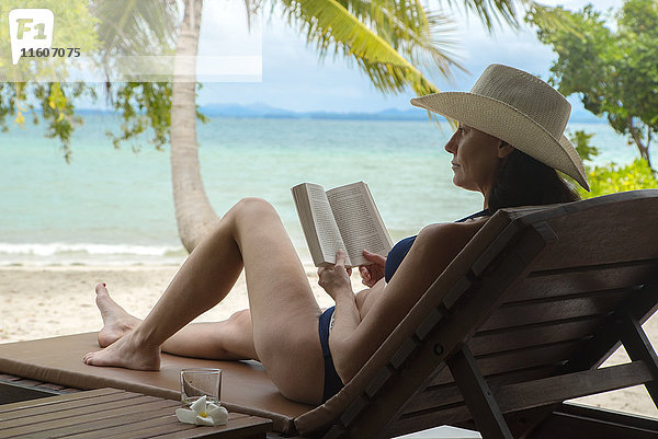 Frau liest Buch am tropischen Strand
