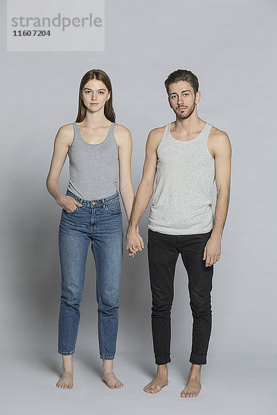 Porträt eines Paares  das sich an den Händen hält  während es auf grauem Hintergrund steht