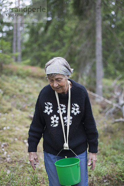 Seniorin mit Eimer im Nacken beim Gehen auf dem Hügel