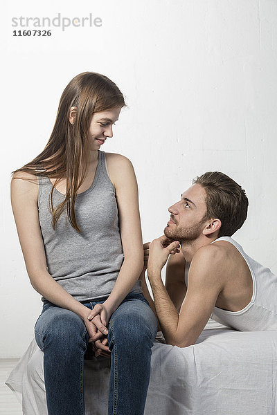 Lächelnder Mann  der die Freundin ansieht  während er sich auf dem Sofa vor weißem Hintergrund ausruht.