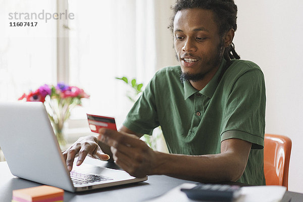 Junger Mann online einkaufen durch Laptop und Kreditkarte zu Hause