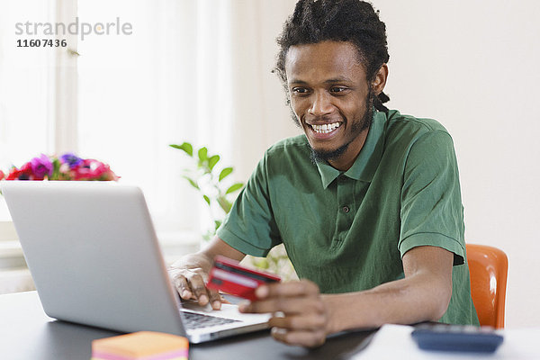Glücklicher Mann online einkaufen durch Laptop zu Hause