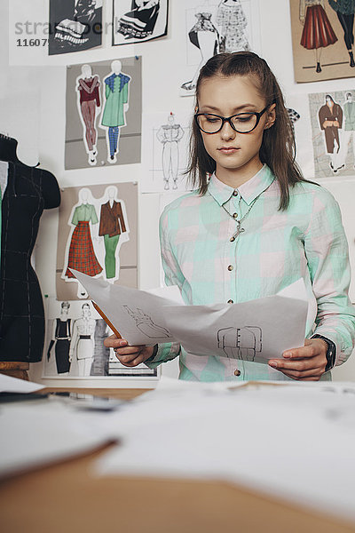 Schöne Modedesignerin beim Betrachten von Skizzen Werkbank im Studio