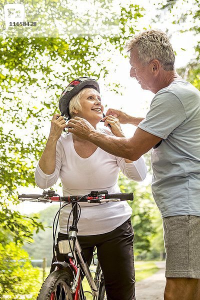 Ältere Frau auf dem Fahrrad  älterer Mann  der mit Helm hilft.