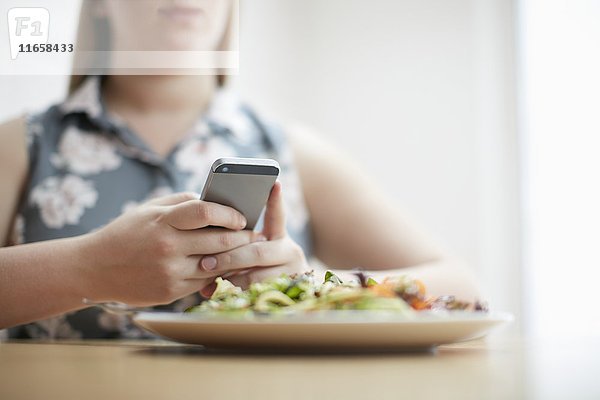 Frau mit Smartphone und einem Teller mit Essen im Vordergrund.