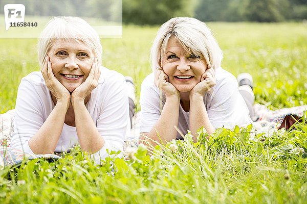 Zwei Frauen liegen im Gras und haben die Hände am Kinn.