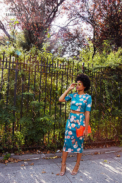 Junge weibliche Mode-Bloggerin mit Afro-Haaren wartet auf dem Bürgersteig eines Parks  New York  USA