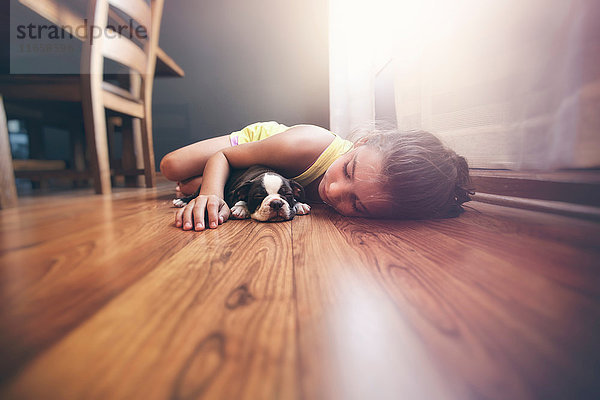Auf dem Boden liegendes Mädchen mit schlafendem Boston-Terrier-Welpen