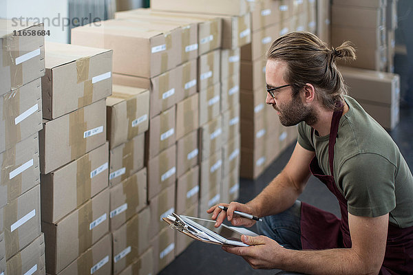 Mann benutzt digitales Tablett  um verpackte Produkte im Fabriklager zu markieren