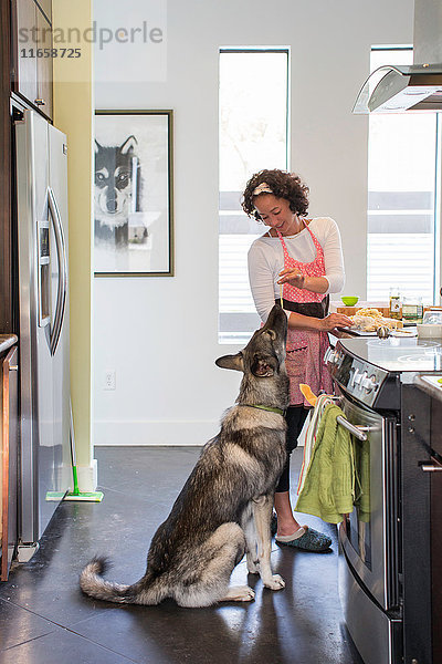 Reife Frau kocht in der Küche und füttert ihren Haushund mit Nudeln